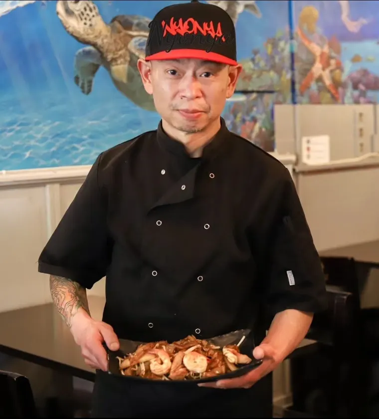 Chef Kit holding a plate of char kway teow in the restaurant
